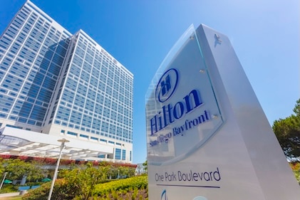 View from the ground looking up at a Hilton Hotel tower and sign against a clear blue sky.