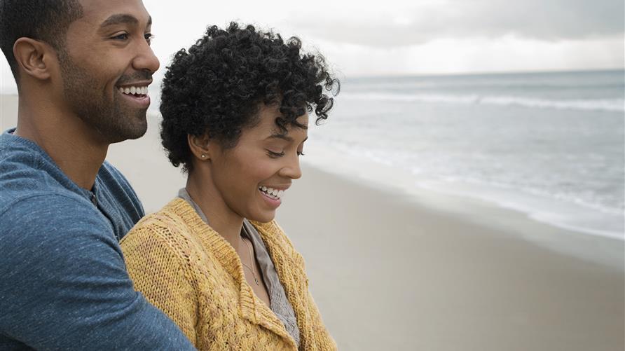 Couple holding each other on the beach staring out at the ocean hopefully. 