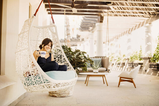 Woman reading a booking and drinking coffee at La Pacifica by Hilton Club in Los Cabos, Mexico. 