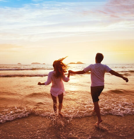 Couple jumping into the waves at the beach during sunset.