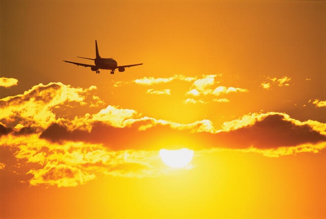 Plane flying off into the orange glow of the sun.