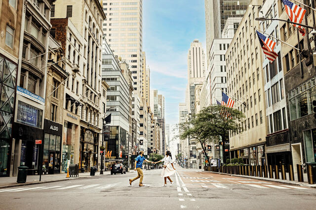 Couple walking hand in hand across a New York City street lined with skyscrapers and looking in awe.