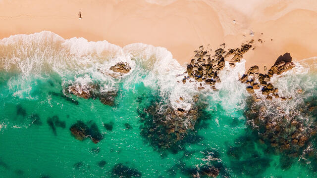 Aerial shot of the Sea of Cortez washing ashore a golden Los Cabos beach, Mexico. 