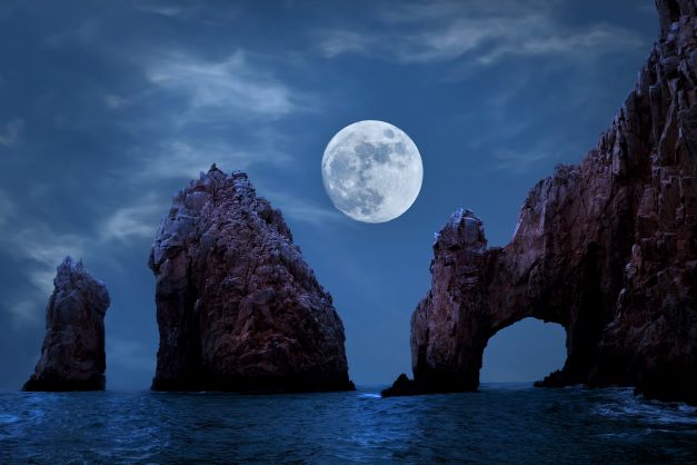 Full moon glowing over the Arch of Cabo San Lucas, nighttime, Mexico.