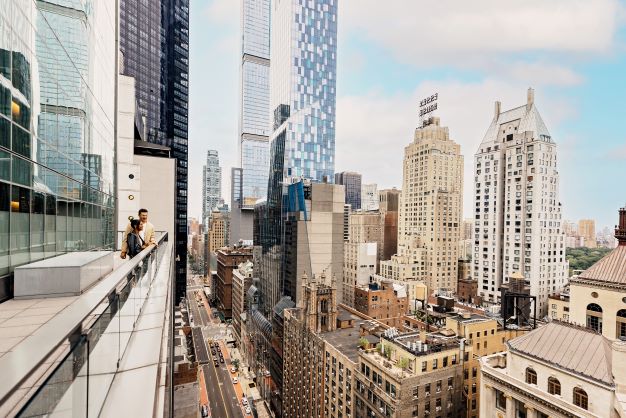 A couple stands on a balcony looking out on the New York City skyline