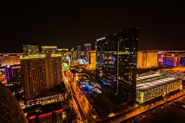 Aerial view of the mirrored exterior of Elara, a Hilton Grand Vacations in Las Vegas at night with the nearby Strip's neon lights