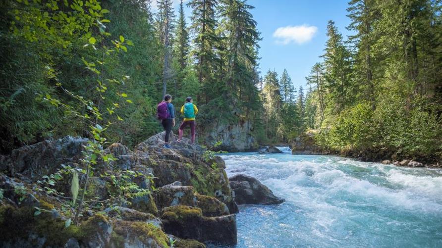 Two hikers stand at the rocky bank of a river near Whistler, Canada