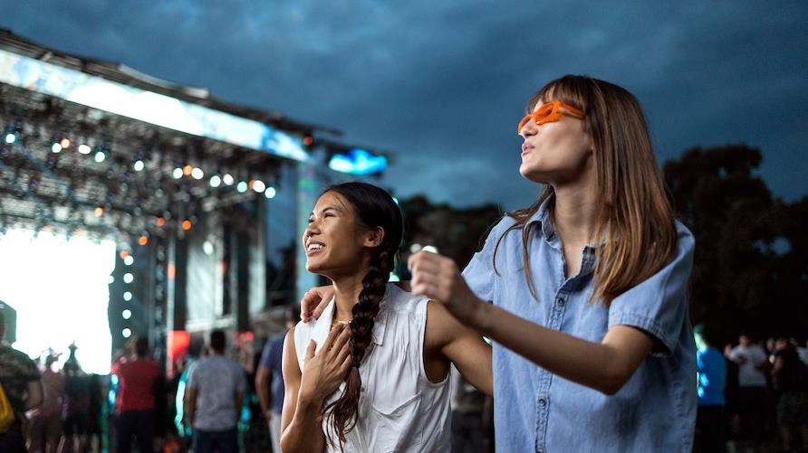 Two women dance in front of a stage at a music festival