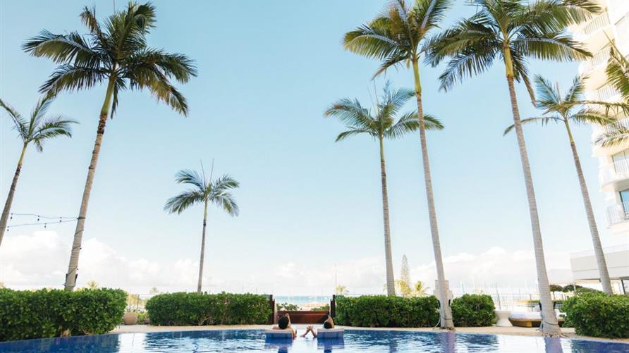 A couple lounges at the pool at The Modern, a Hilton Vacation Club in Honolulu, Oahu, Hawaii