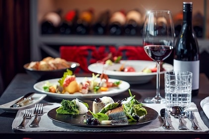 Table set for fine dining in Las Vegas including a glass of wine and colorful plates of appetizers with wine rack seen in the background. 