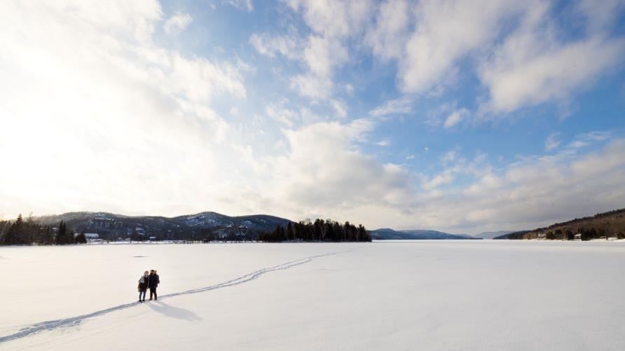 Beautiful aerial image, couple, holding hands, walking, snow-covered vista, blue skies overhead,  Mont-Tremblant, Québec, Canada.