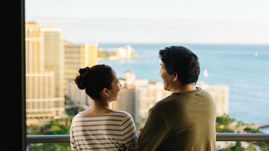 A couple enjoys the view from the balcony of a Suite at The Grand Islander, a Hilton Grand Vacations Club in Oahu, Hawaii
