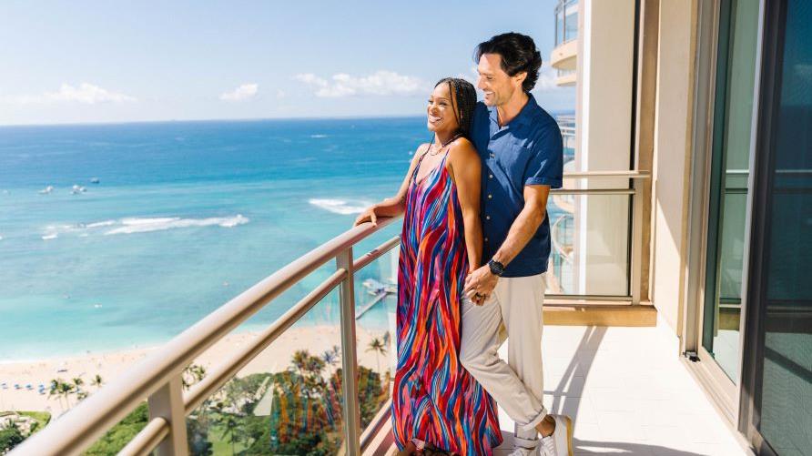 Couple enjoying ocean views, balcony, Hilton Grand Vacations beachfront resort. 