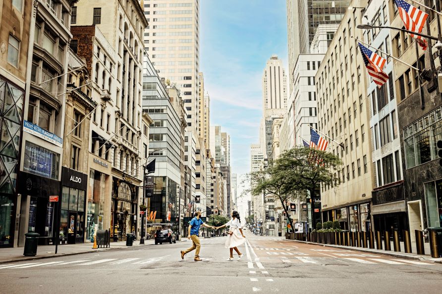 Couple walking, hand in hand, empty urban street, blue skies peek through buildings, New York, New York. 