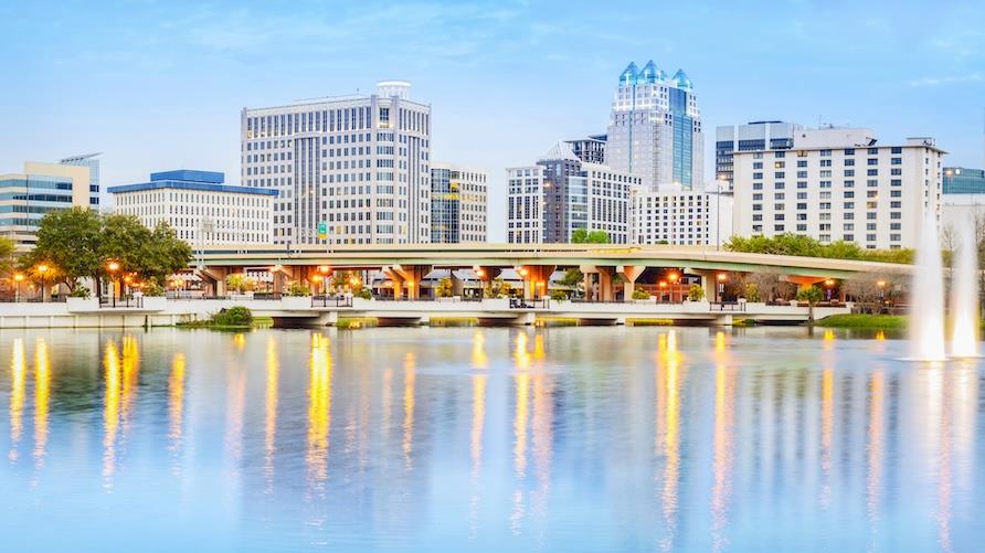 Eye-level view of the Orlando city skyline with Lake Eola in the foreground under blue skies.