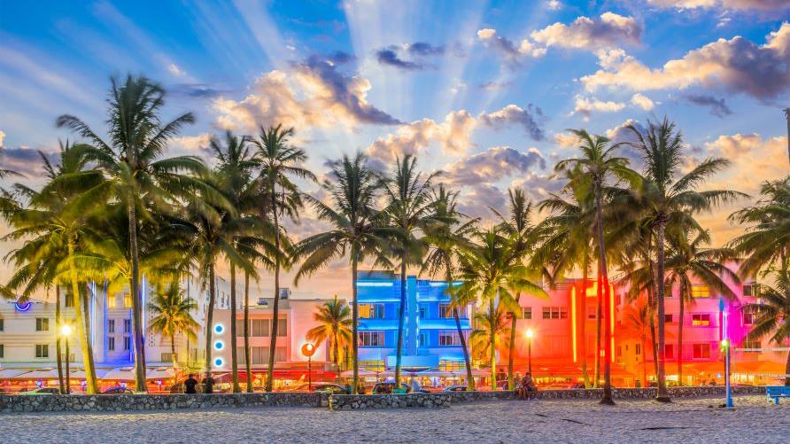 Art Deco buildings a glow behind palm trees, South Beach, Miami, Florida. 