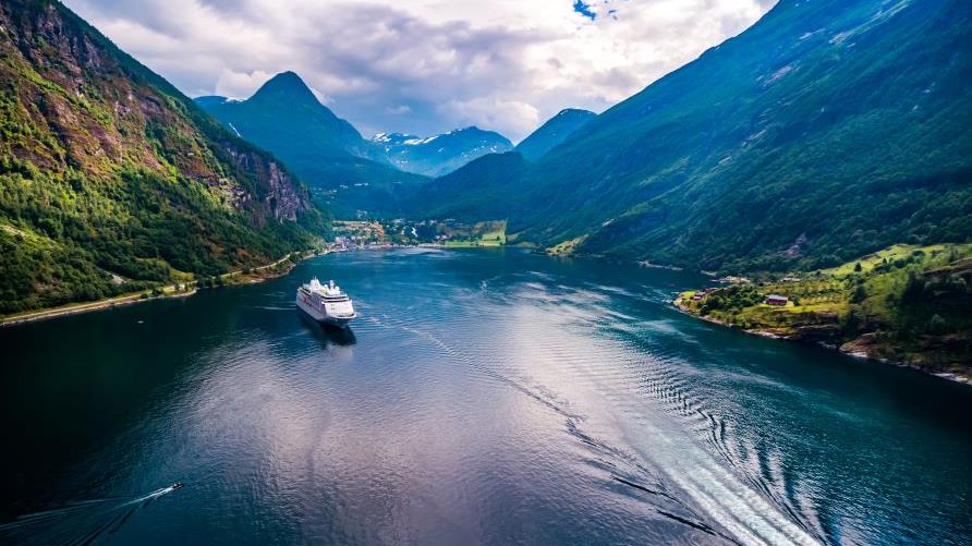 Stunning aerial image, cruise ship sailing through mountain-lined waterway, calm waters, blue sky. 