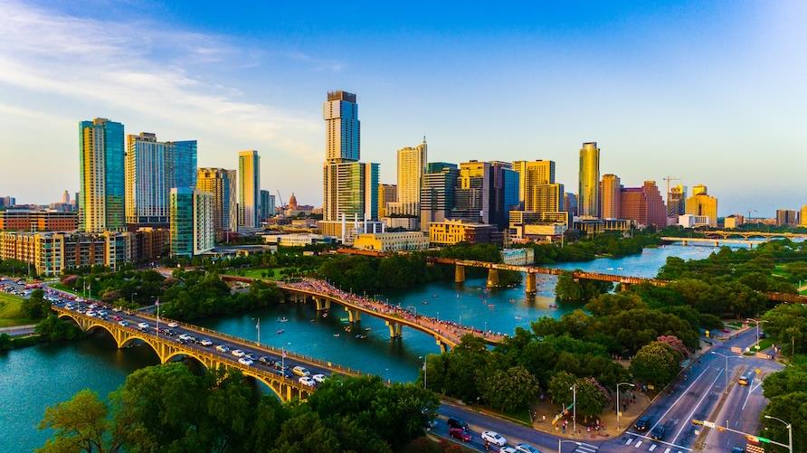 Drone view of the Austin Texas skyline during the golden hour. The river and several bridges are in the foreground, with golden-lit skyscrapers beyond.