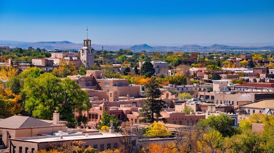 Downtown Santa Fe, New Mexico skyline view during autumn, with a beautiful variety of fall colors on lush trees all around and mountains in the distance.
