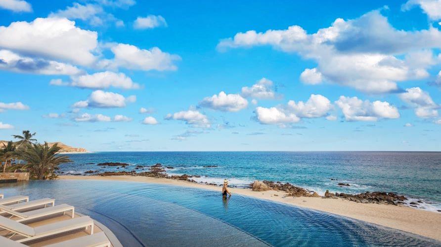 Beautiful panoramic image, woman in infinity pool gazing out to the Sea of Cortez, clear blue skies and blue waters, La Pacifica Los Cabos, a Hilton Club, Mexico. 