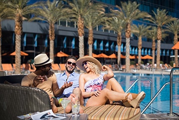 Group laughs together as they sit poolside with their drinks.