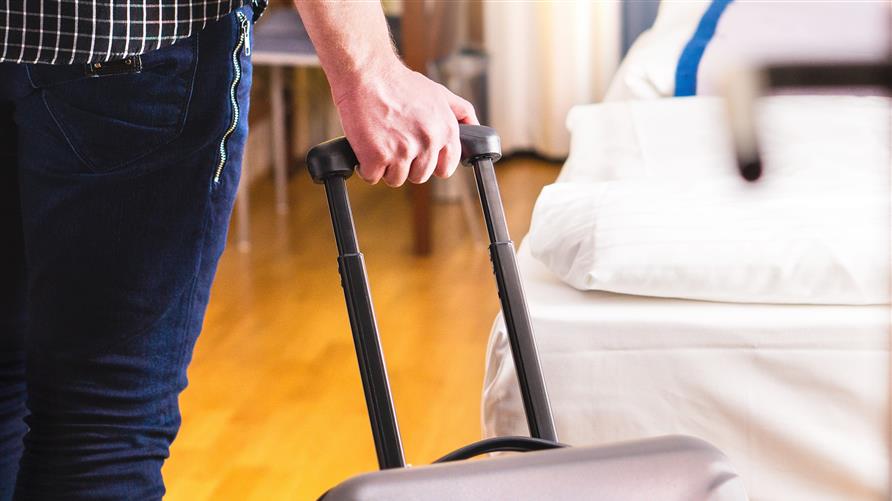 A close up shot of a traveler with his hand on the handle of his suitcase. 