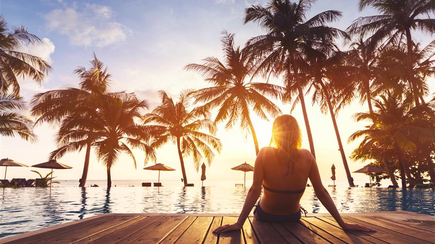 Woman sitting on the edge of an palm tree lined infinity pool overlooking the ocean. 