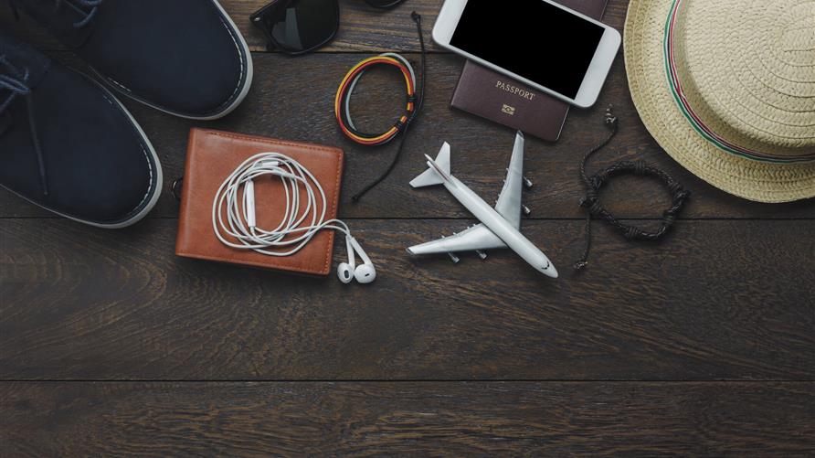 Flat lay shot of travel items including passport, shoes, hat and phone. 
