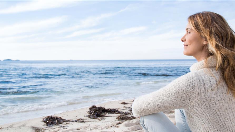 Woman gazing out to the ocean while sitting on the beach. 