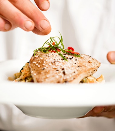 Close-up of chef sprinkling herbs on a bowl of salmon