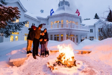 A group standing in the snow by a bonfire in the early evening