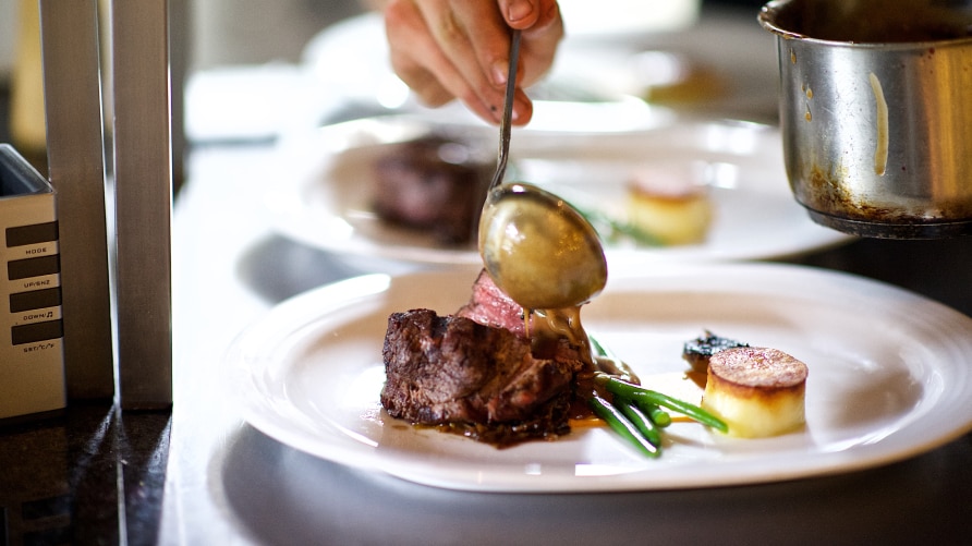 Chef's hand ladling sauce on filet mignon on a gourmet plate
