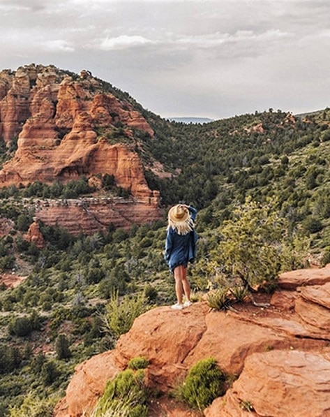 A hiker stands on an Arizona red rock and looks upon the mountains and desert scrub.