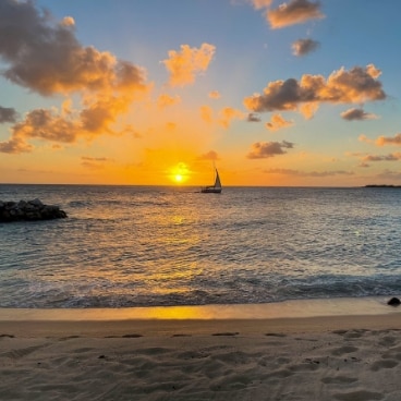 The sun sets orange on the Caribbean waters as a boat sails across the horizon.