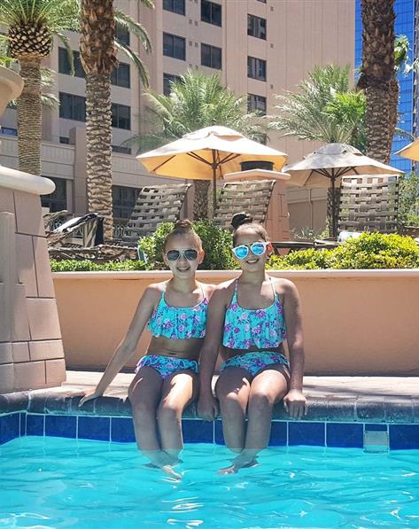 Girls in matching swim suits sit on the edge of a pool on a sunny day.
